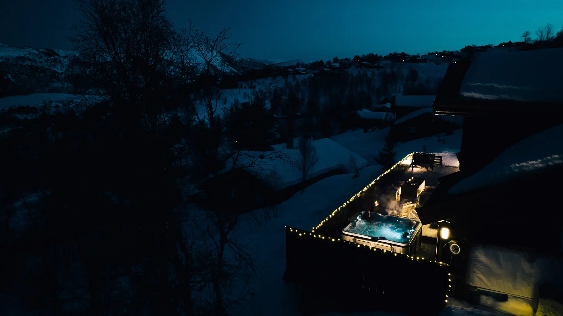 A lit hot tub beside a snowy cabin at night